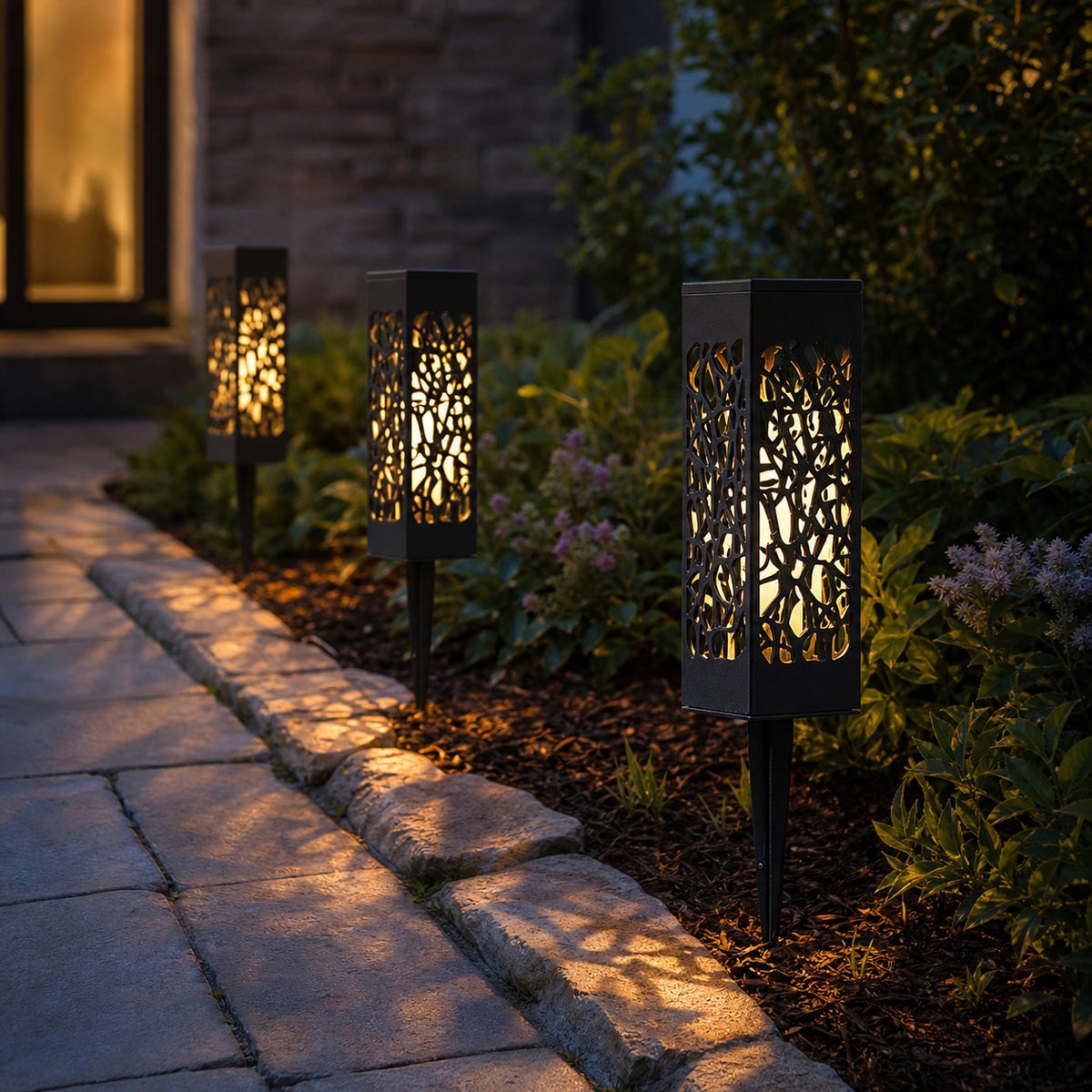 Solar filigree pathway lights casting patterned light along a garden border
