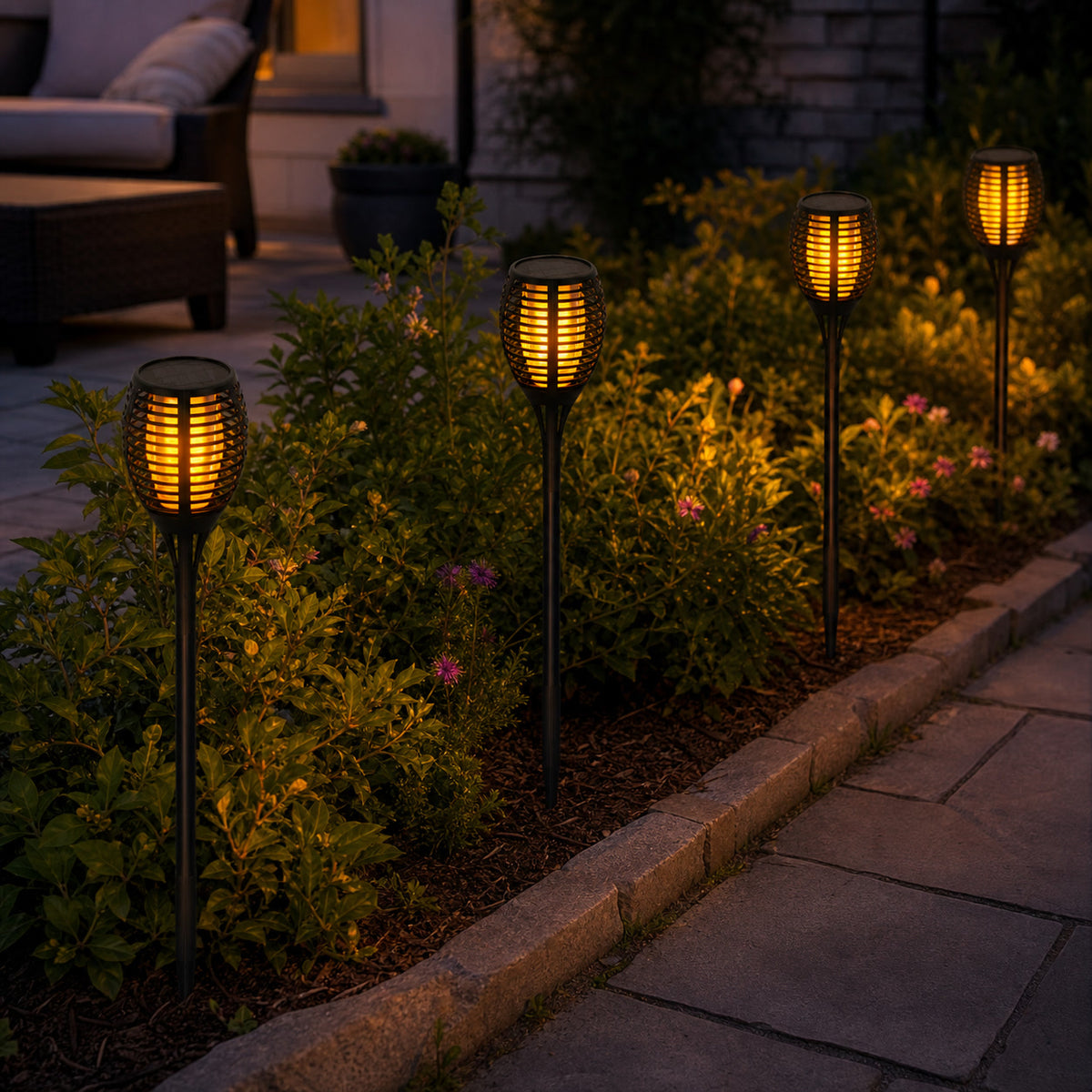 Solar torch garden lights adding warm ambience along a planted patio border